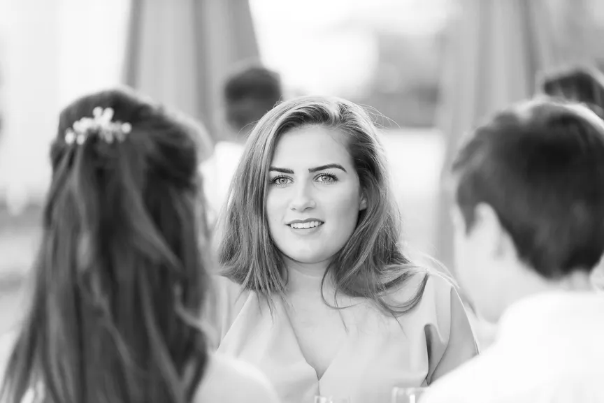 Black and white photo of a young woman with long hair smiling and looking at two people in front of her.