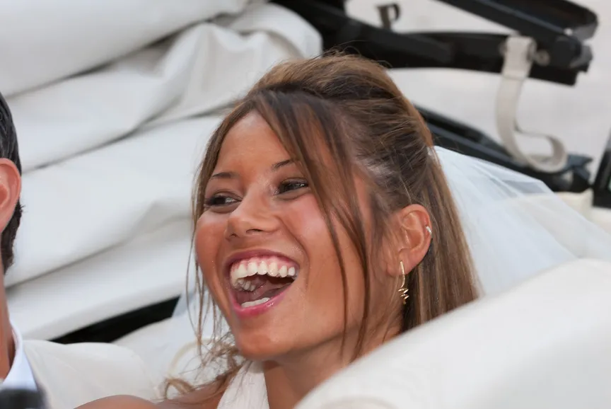 Close-up of a smiling bride with brown hair and gold earrings, wearing a white veil.