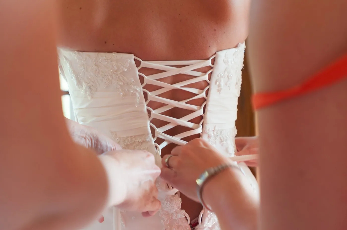 Close-up of hands lacing up the back of a white wedding dress with delicate embroidery.