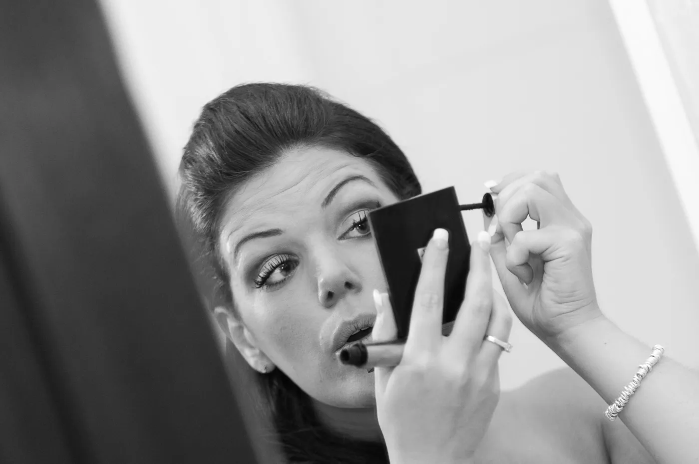 Woman applying mascara while looking into a small handheld mirror.