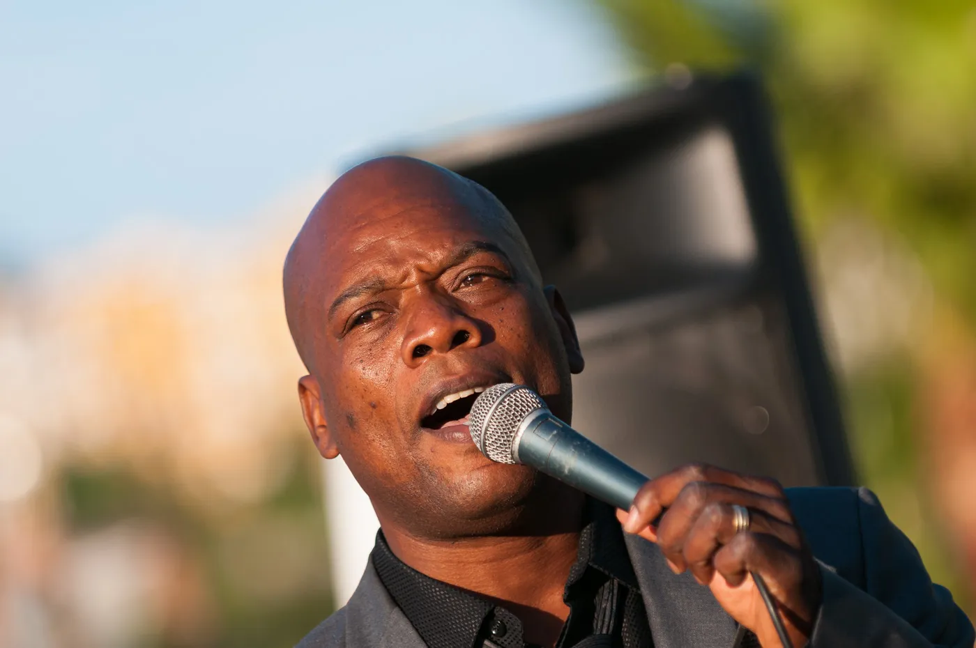 Close-up of a man speaking into a microphone outdoors with blurred background.
