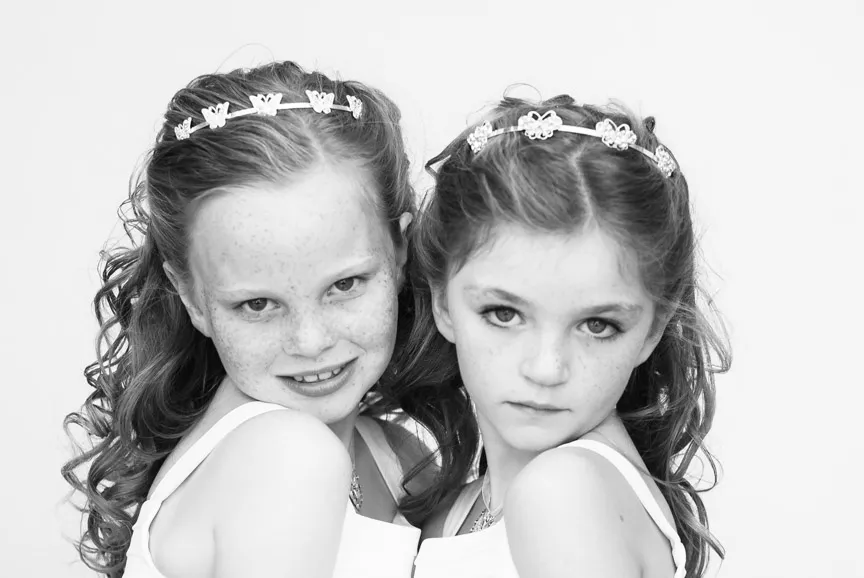 Black and white portrait of two young girls with curly hair and floral headbands looking towards the camera.