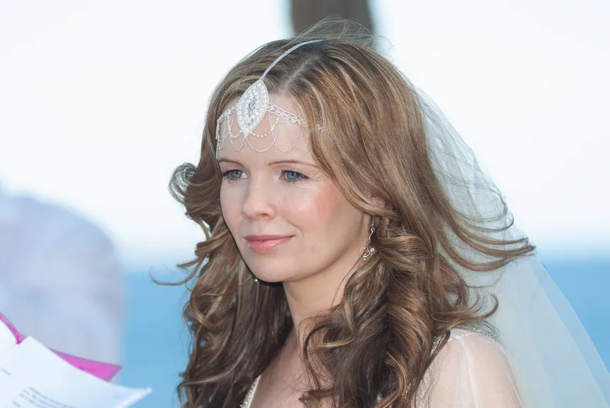 Bride with long curly hair wearing a delicate jeweled headpiece and veil, looking serene.