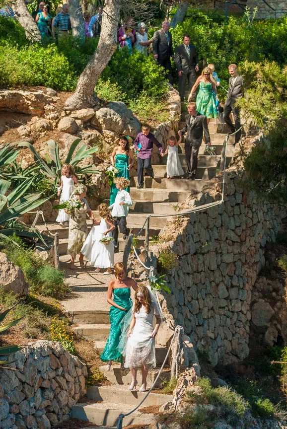 Wedding party walking down outdoor stone steps surrounded by greenery and rocky walls.