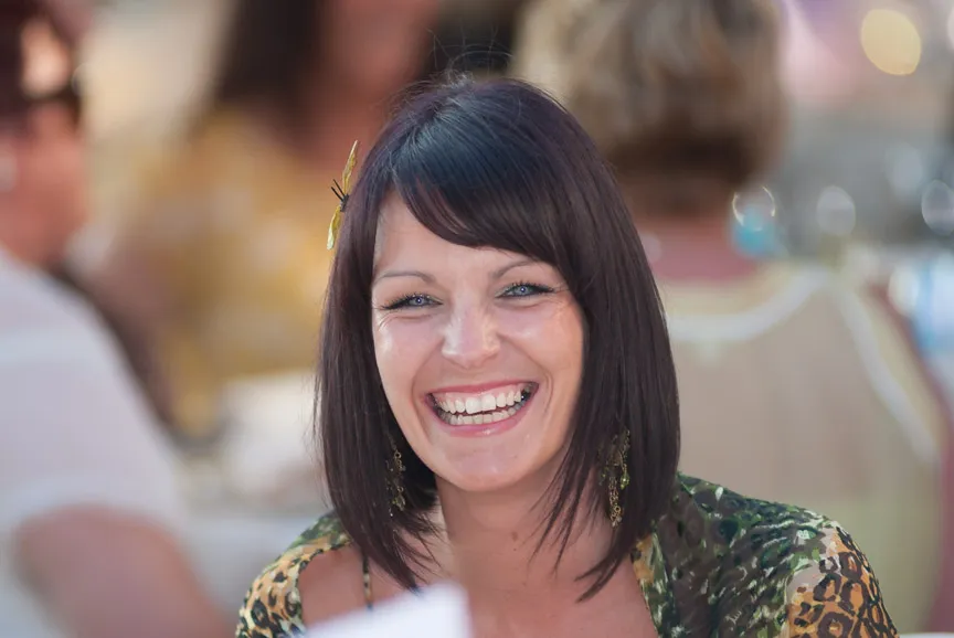 Smiling woman with dark hair wearing a patterned top and dangling earrings, with blurred people in the background.