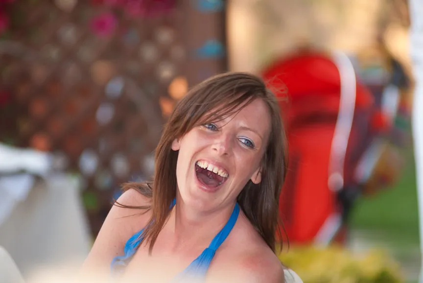 Smiling woman with brown hair wearing a blue halter top, outdoors with blurred background.