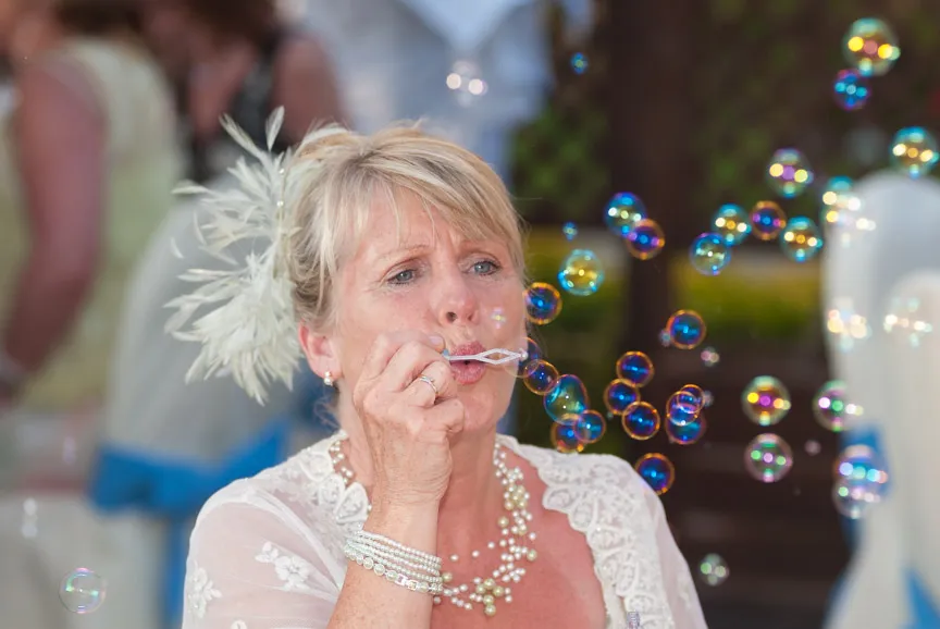Blonde woman wearing lace dress and pearl necklace blowing colorful soap bubbles.