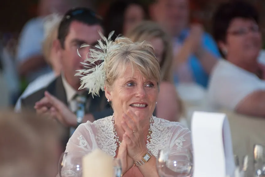 Smiling woman with a feathered hair accessory clapping at an event.