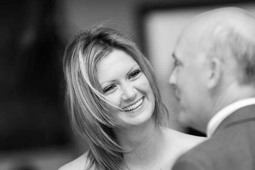 Black and white photo of a smiling woman with shoulder-length hair looking at a man in a suit.