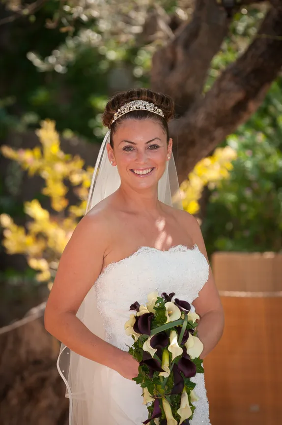 Smiling bride in white strapless gown and jeweled headband holding a cascading bouquet of white and dark purple calla lilies.