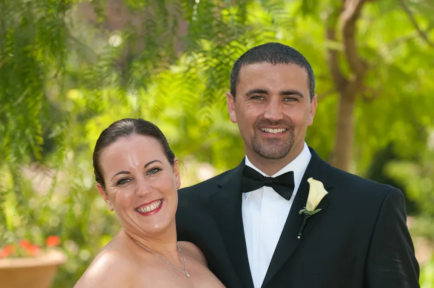Smiling bride and groom posing outdoors with green foliage in the background.