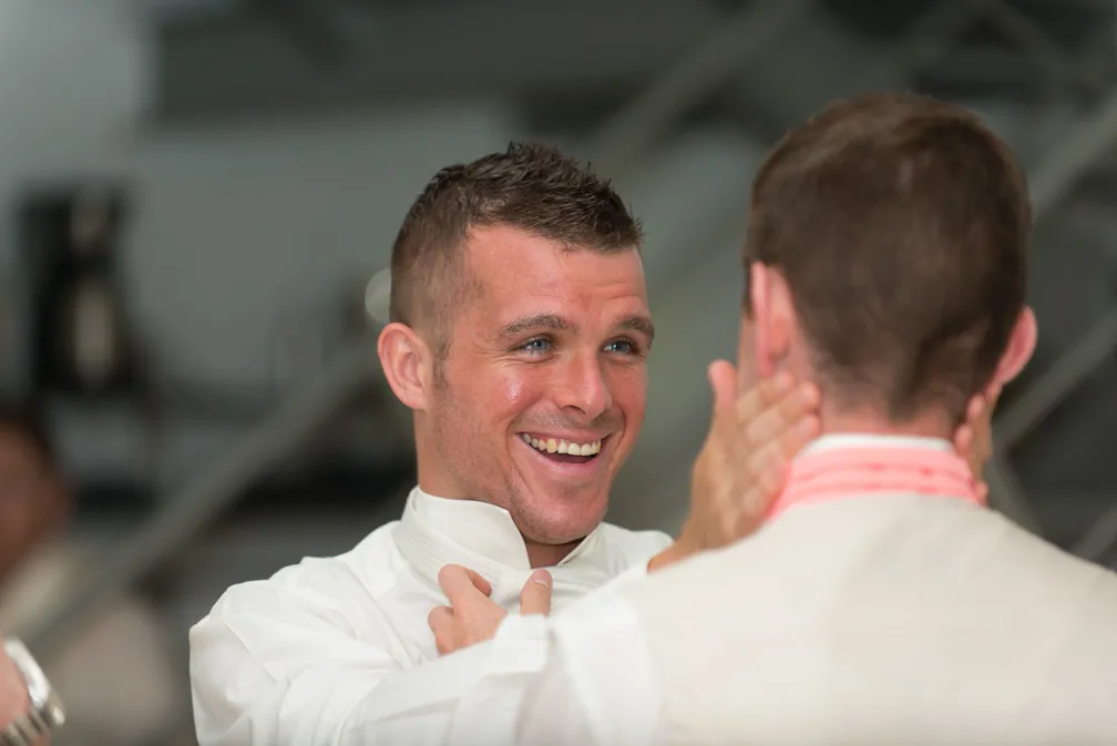 Smiling man adjusting another man's collar in a candid indoor moment.