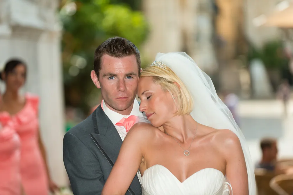 Bride resting her head on the groom's shoulder as they pose together outdoors on their wedding day.