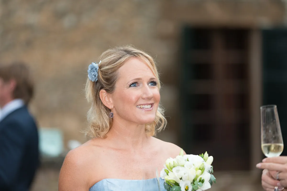 Smiling woman in a light blue strapless dress holding a bouquet of white flowers and wearing a blue flower hair accessory.