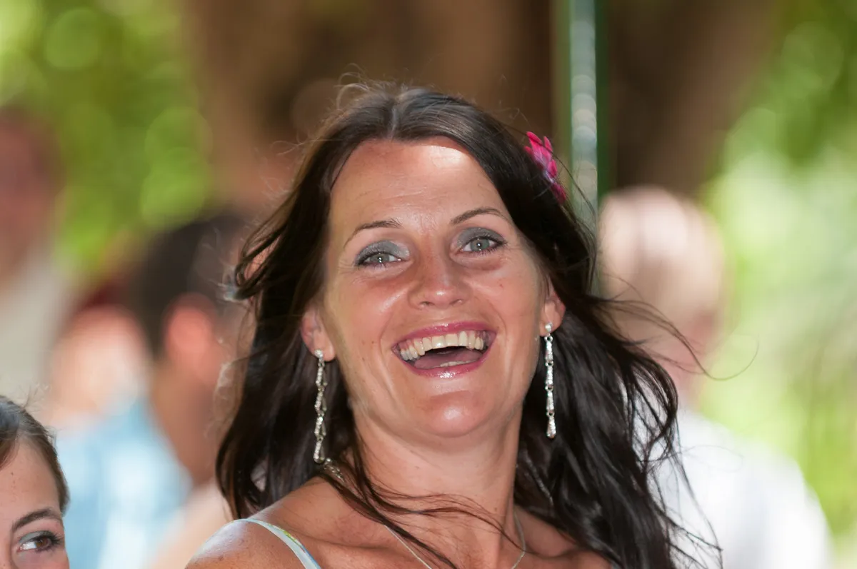 Smiling woman with long dark hair, silver earrings, and a pink flower in her hair.