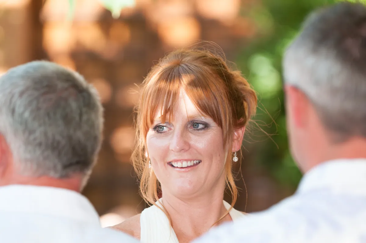 Smiling woman with red hair in an updo, wearing earrings, looking at two men with gray hair in white shirts.