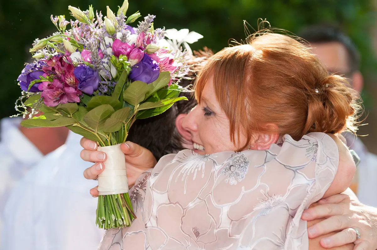 Woman with red hair smiling and hugging someone while holding a colorful bouquet of flowers.