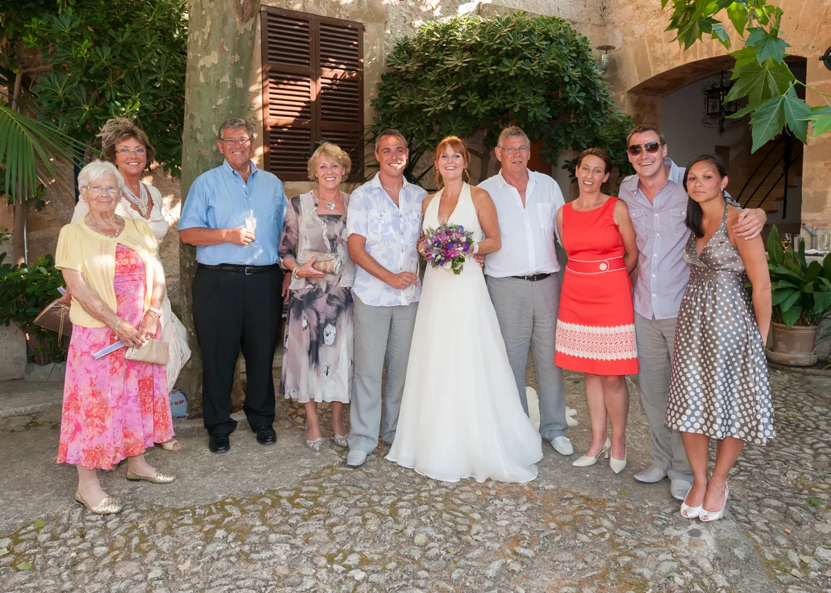 Group of ten people posing together outdoors at a wedding, with the bride in a white gown holding a purple bouquet in the center.