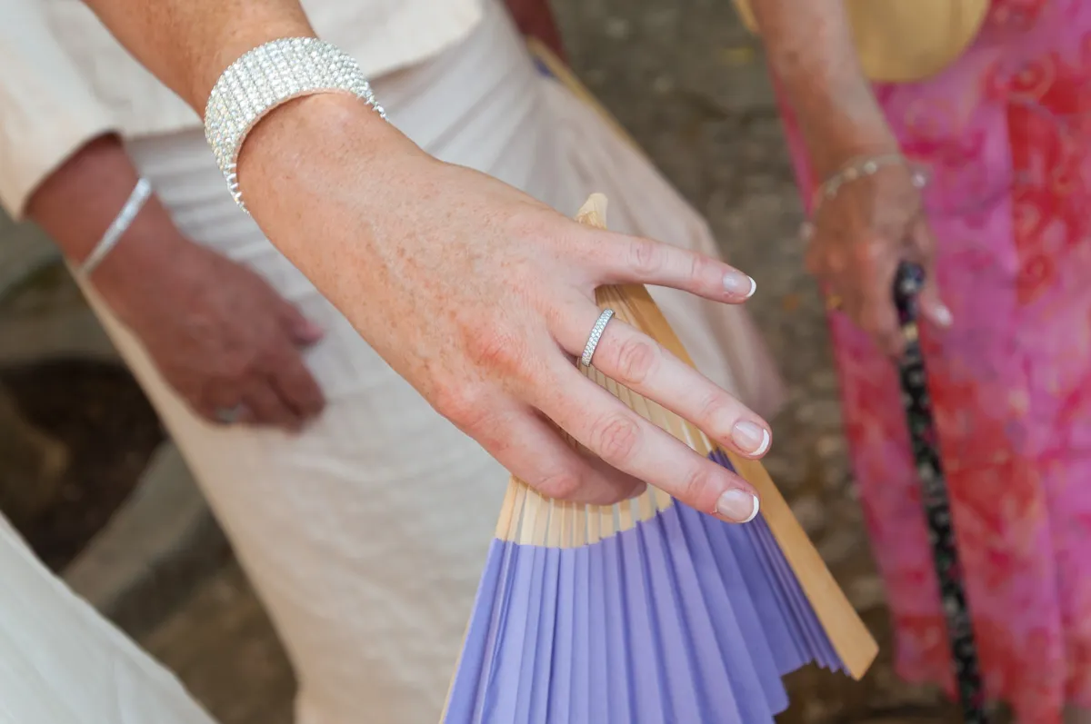 Close-up of a woman's hand wearing a diamond bracelet and ring, holding a folded purple paper fan.