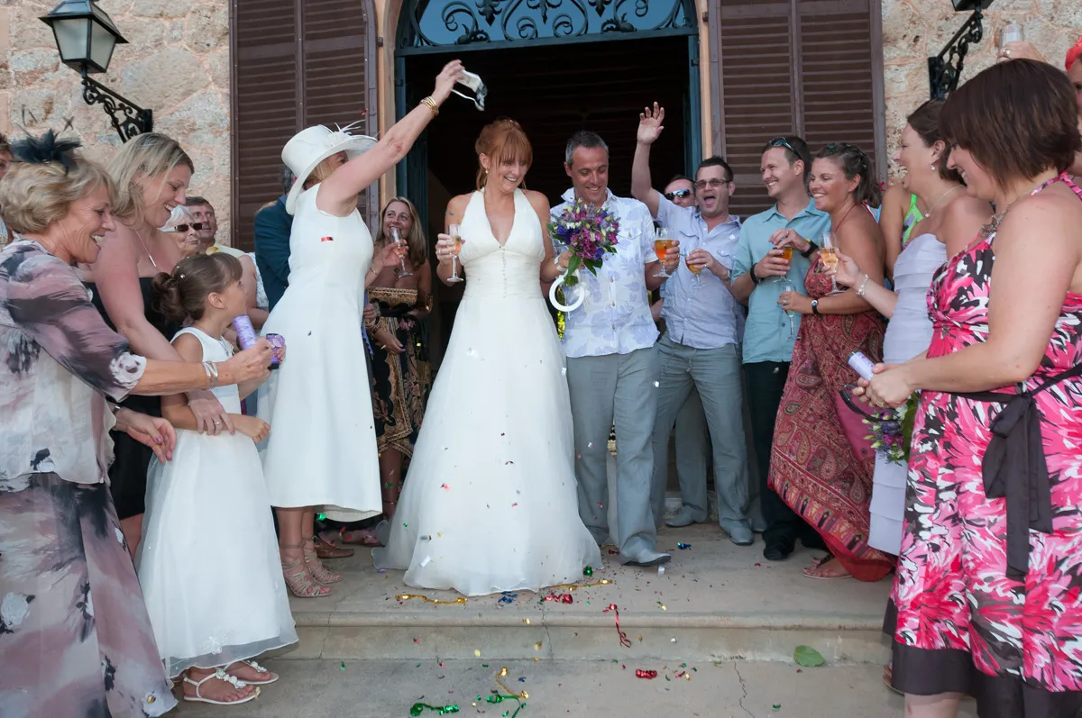 Bride and groom smiling and walking down steps surrounded by guests celebrating and throwing confetti.