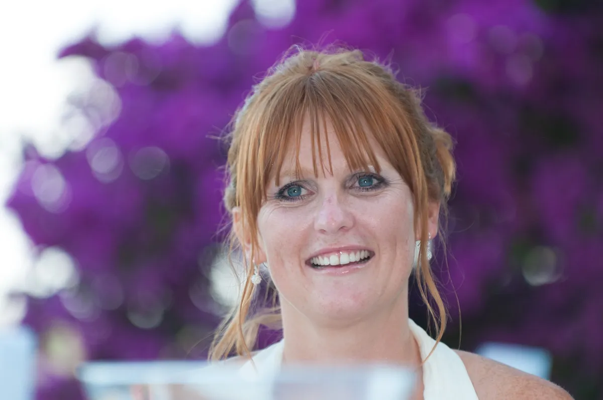 Smiling red-haired woman with blue eyes and earrings, with a blurred purple background.