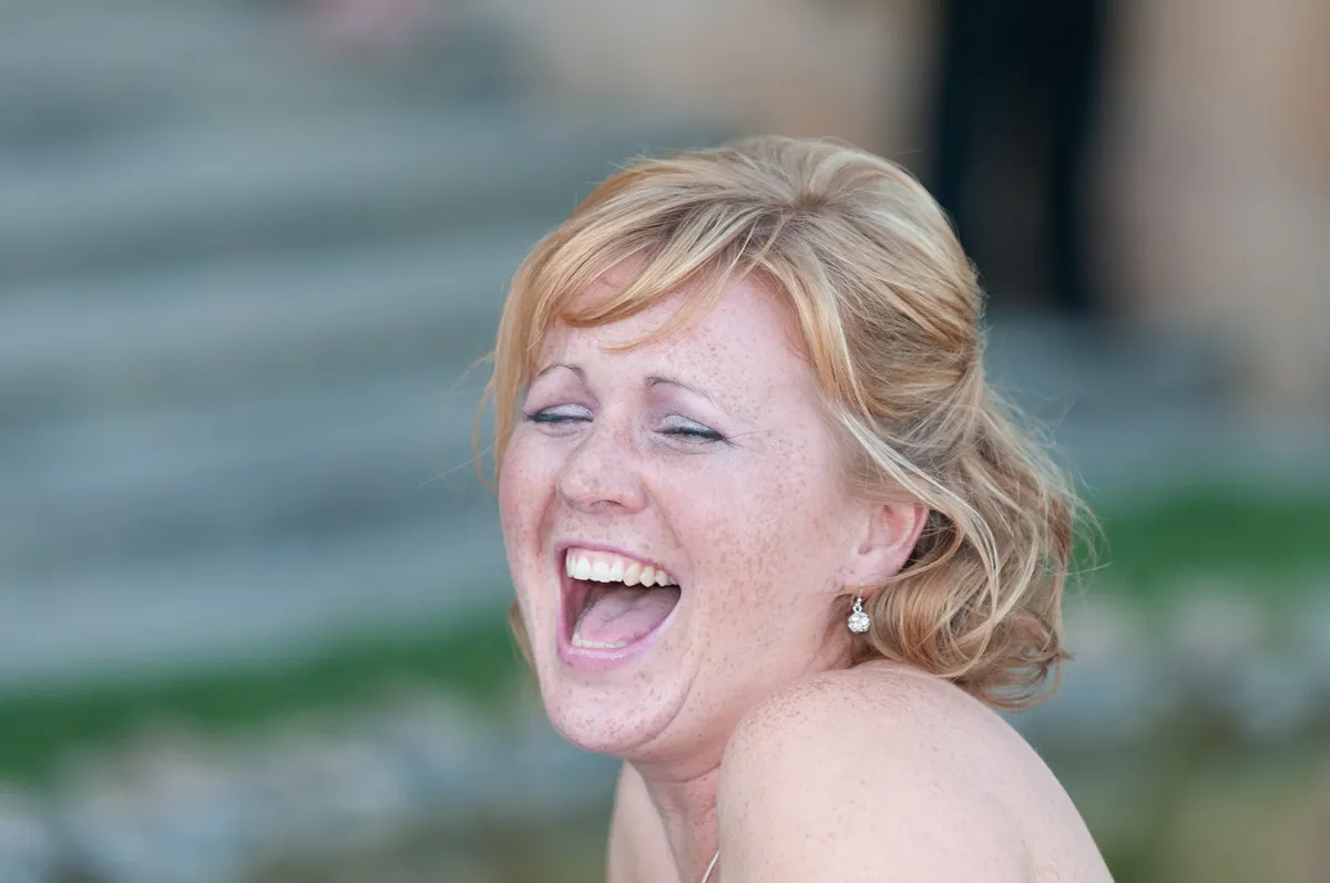 Close-up of a freckled woman with blonde hair laughing joyfully outdoors.