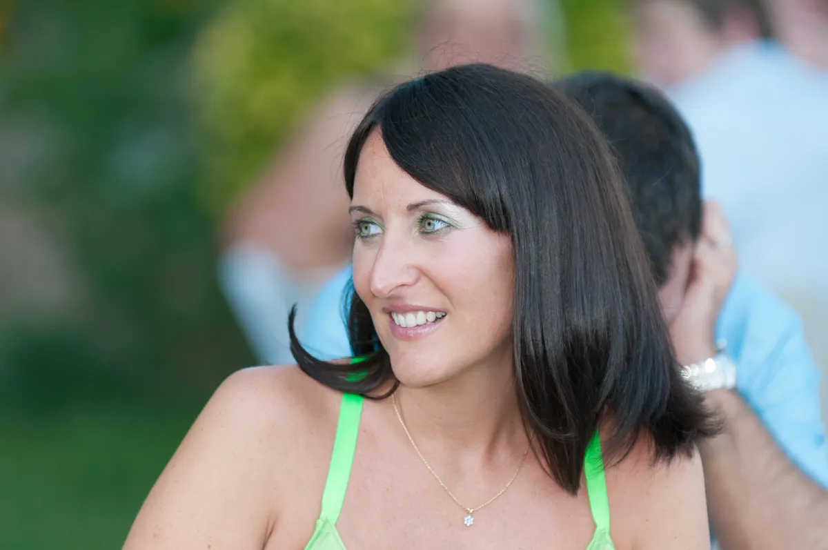 Woman with dark hair wearing a neon green top and a small gold necklace, looking to the side and smiling slightly.