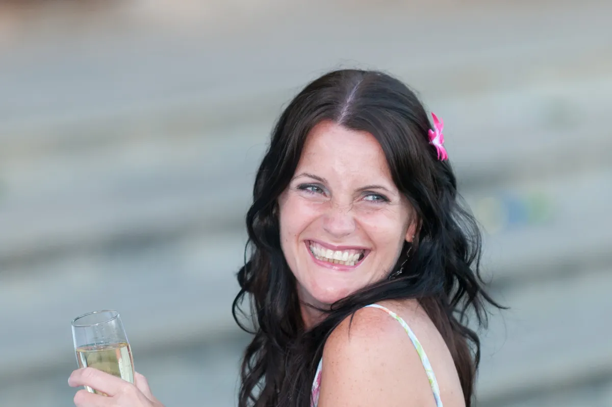 Smiling woman with long dark hair and a pink flower clip holding a champagne glass.