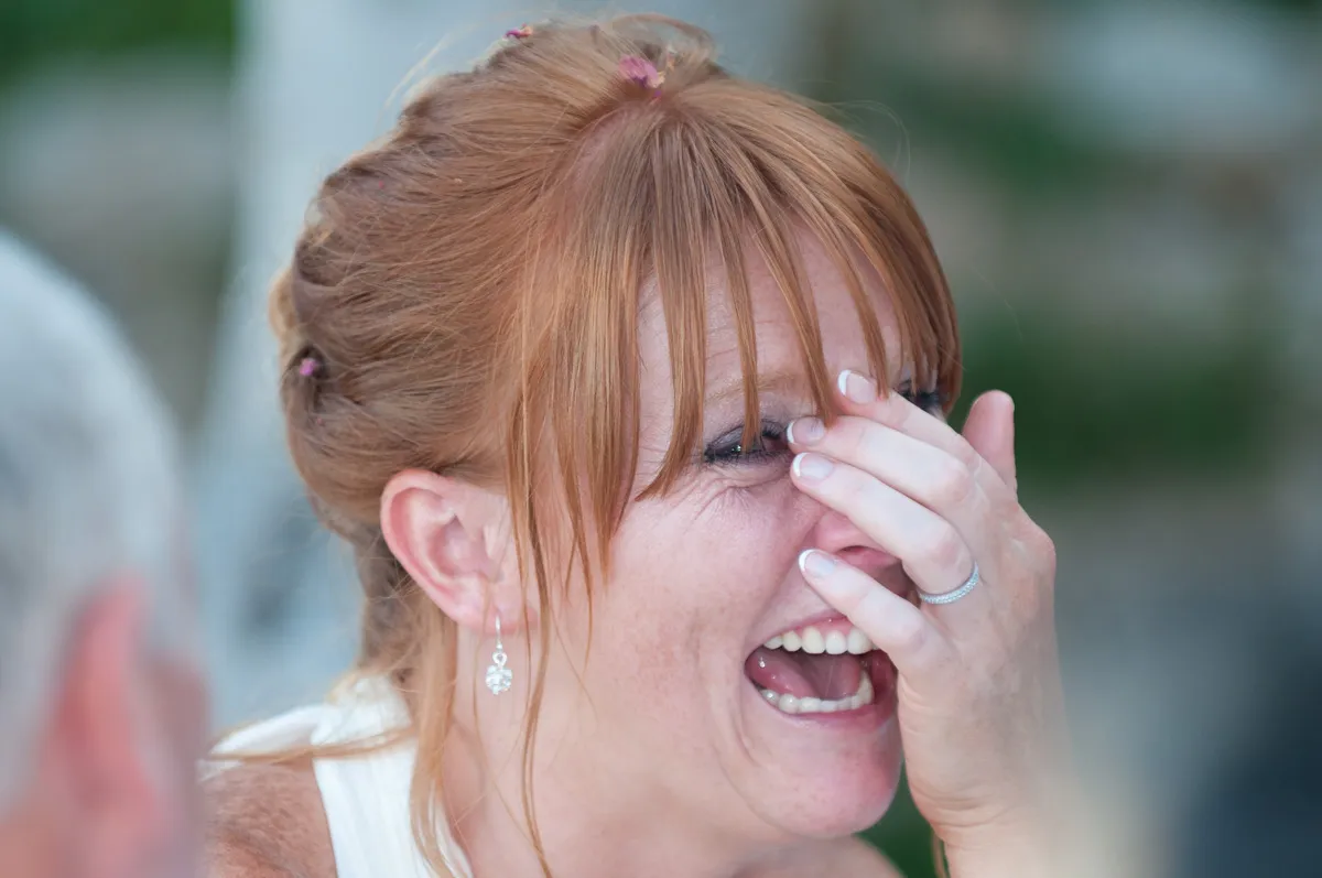Red-haired woman laughing and covering her face with her hand during a joyful moment.