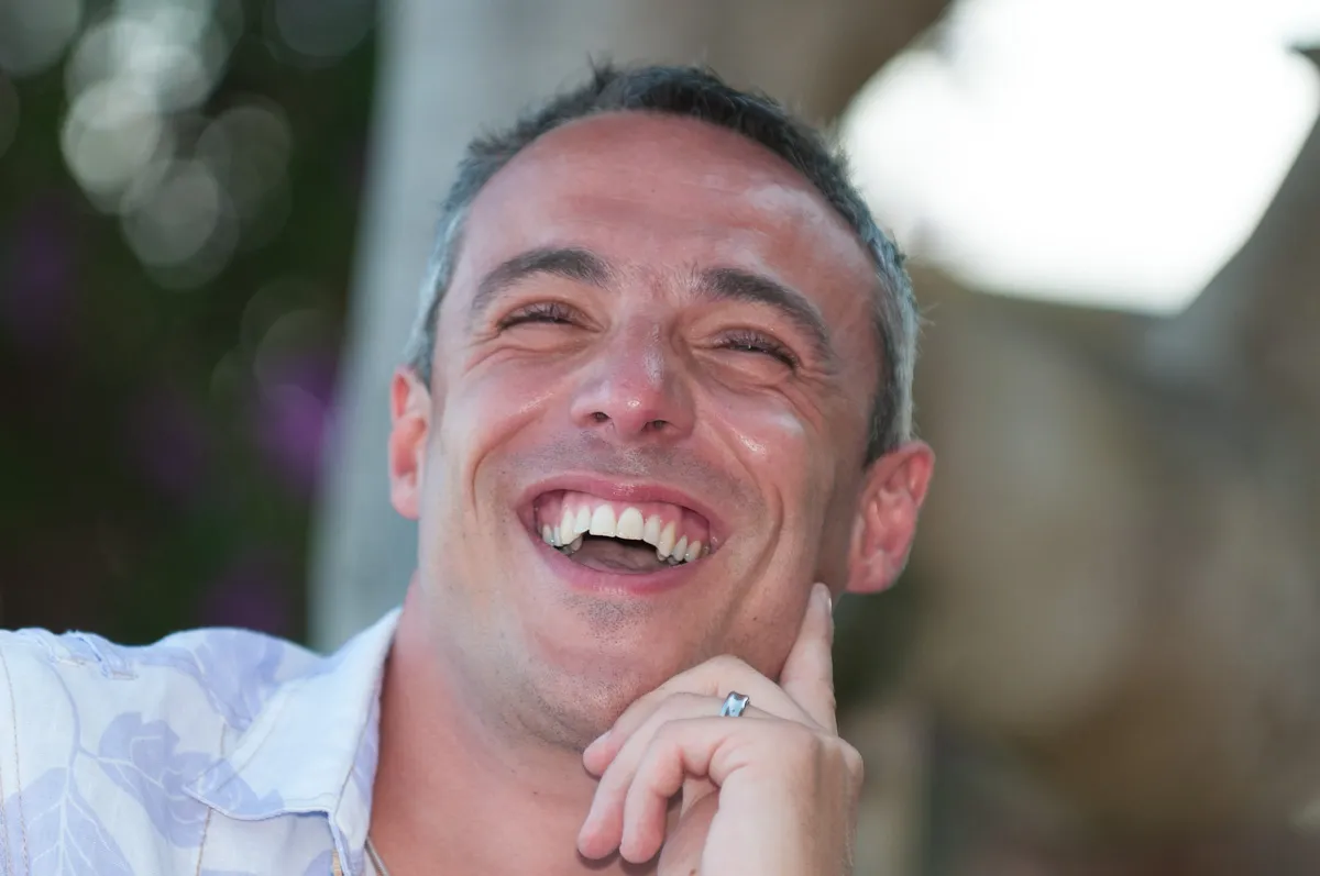 Close-up of a man smiling and laughing with his hand resting on his chin.
