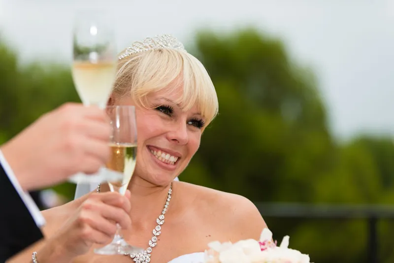 Smiling bride holding a champagne glass during a wedding toast outdoors.