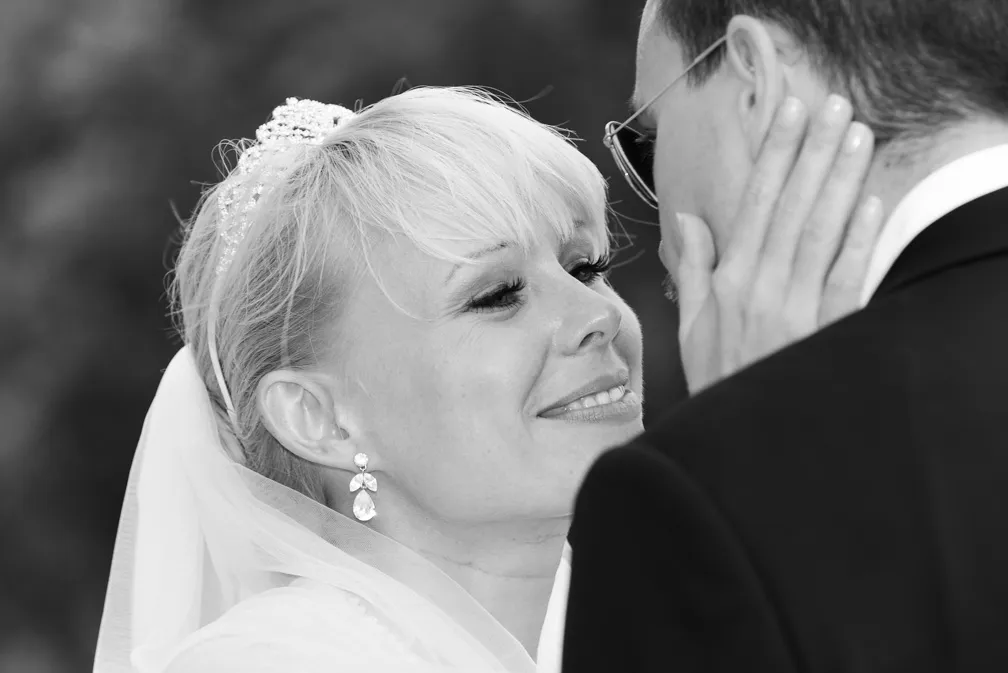 Close-up of a bride smiling tenderly as she touches the groom's face, both dressed in wedding attire.