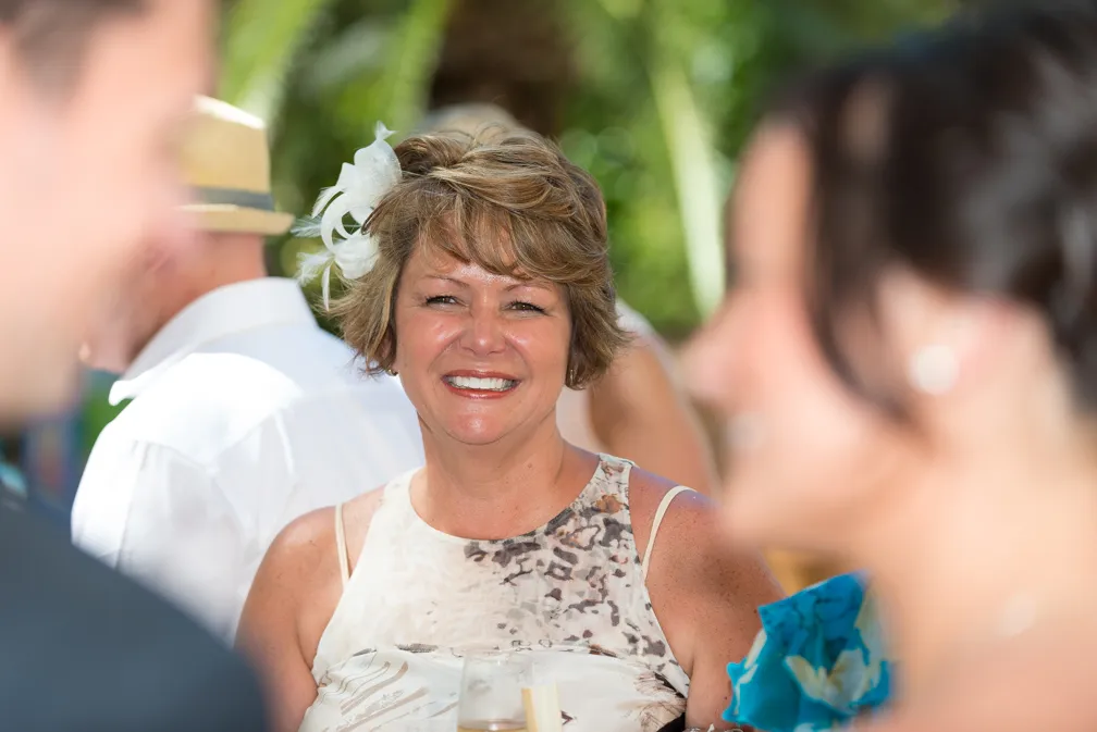 Smiling woman with short hair and a white flower accessory, wearing a patterned sleeveless dress at an outdoor event.