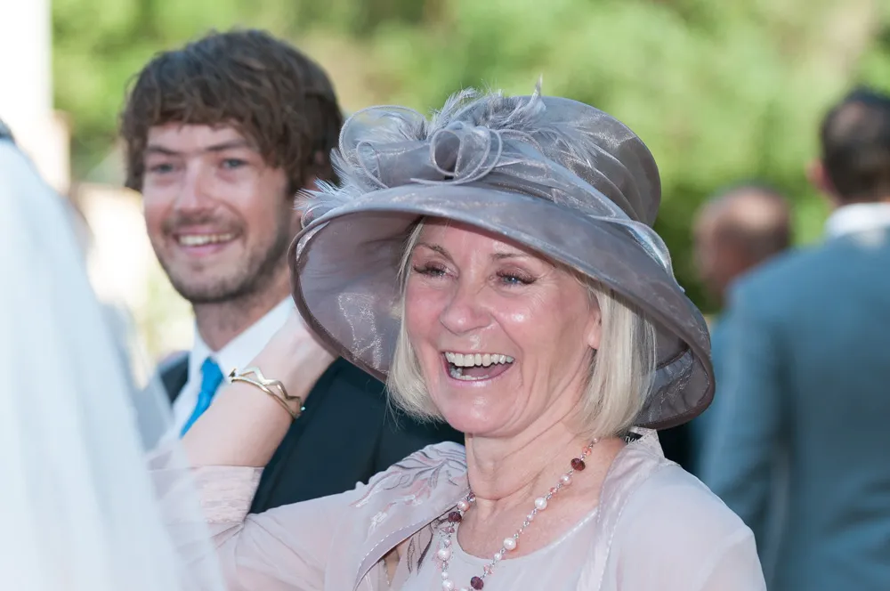 Smiling woman wearing a large decorative gray hat and light pink outfit at an outdoor event.