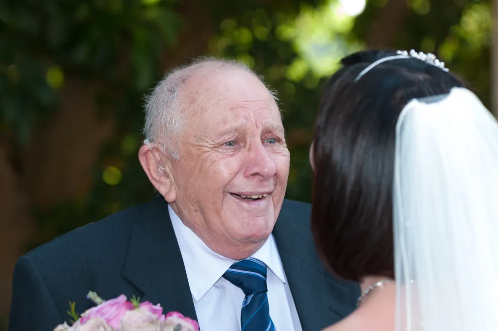 Elderly man in a suit and striped tie smiling warmly at a bride wearing a veil and tiara.
