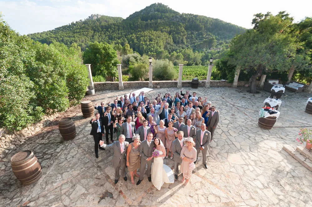 Wedding party posing outdoors on a stone patio with surrounding trees and forested hills in the background.