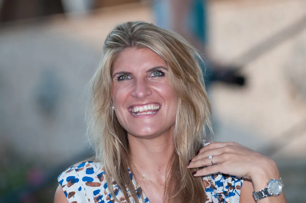 Smiling woman with blonde hair wearing a patterned sleeveless top, a watch, and an engagement ring.