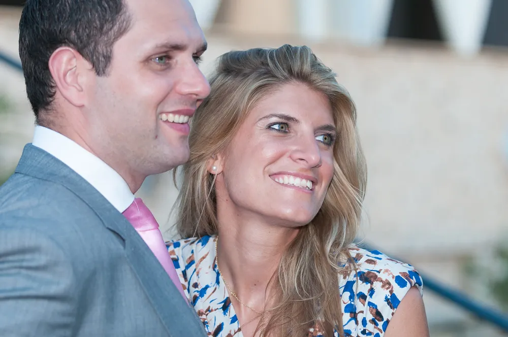 Smiling man in a gray suit and pink tie standing next to a smiling woman with long blonde hair wearing a patterned dress.