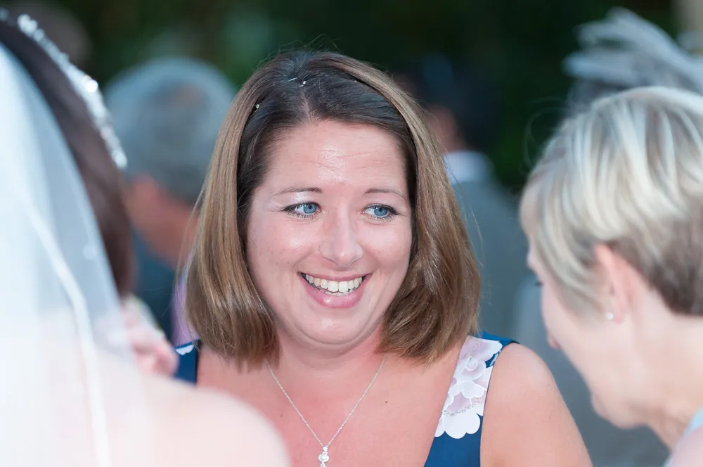 Smiling woman with shoulder-length brown hair wearing a floral dress talking to two other people.