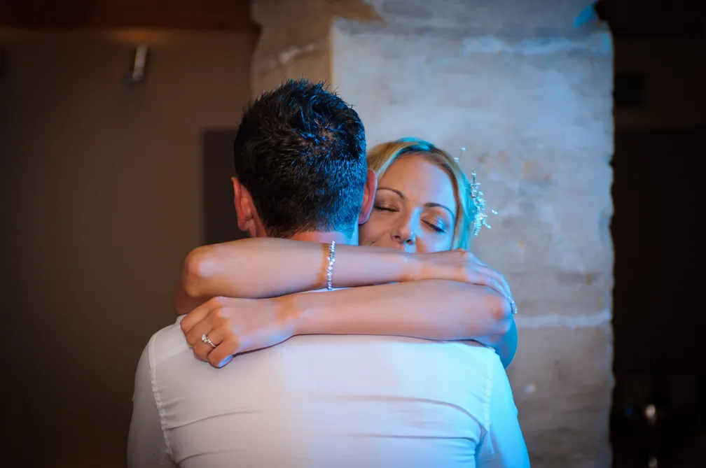 Bride with closed eyes embracing groom wearing a white shirt in a warm, intimate moment.