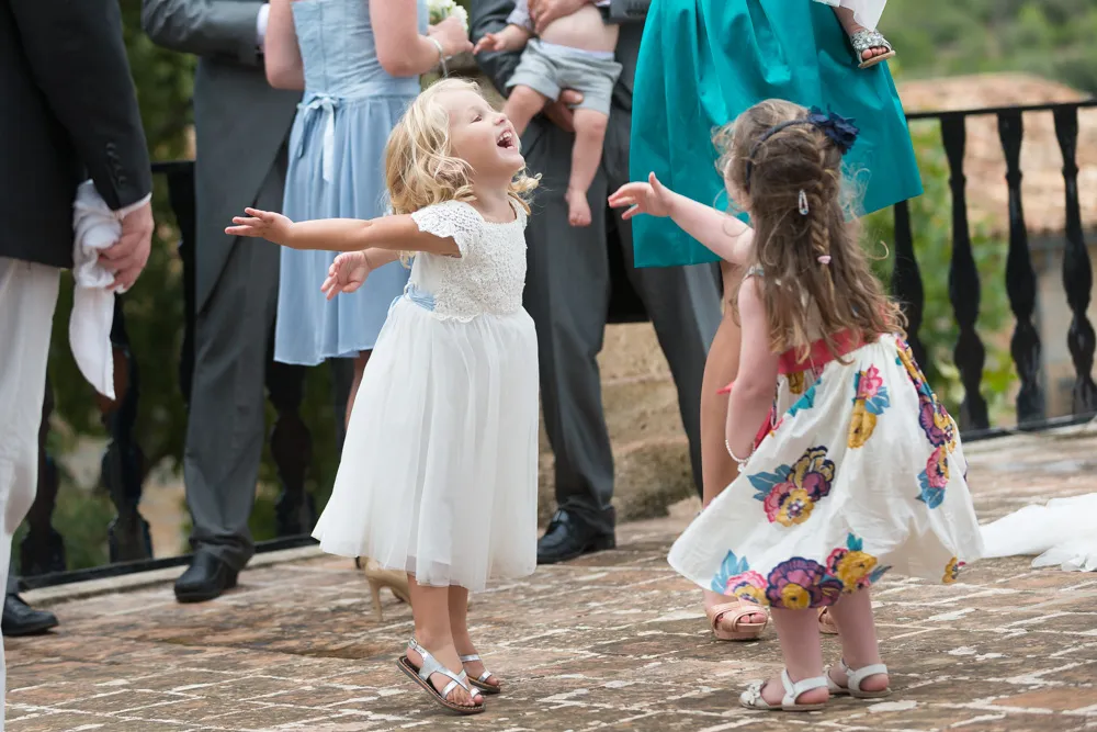 Two young girls in dresses joyfully dancing outdoors on a stone patio during a formal event.