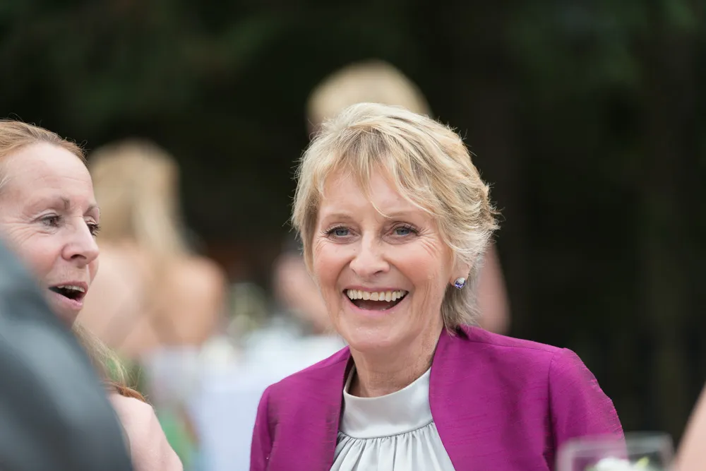 Smiling older woman with short blonde hair wearing a purple jacket and white blouse at an outdoor event.
