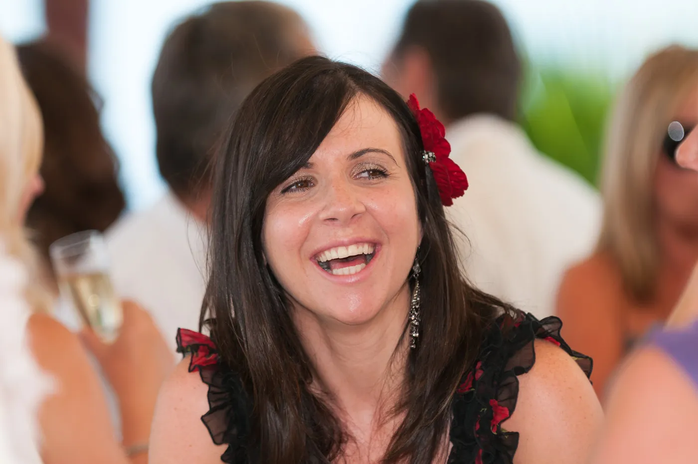 Smiling woman with dark hair and a red flower in her hair at a social event.