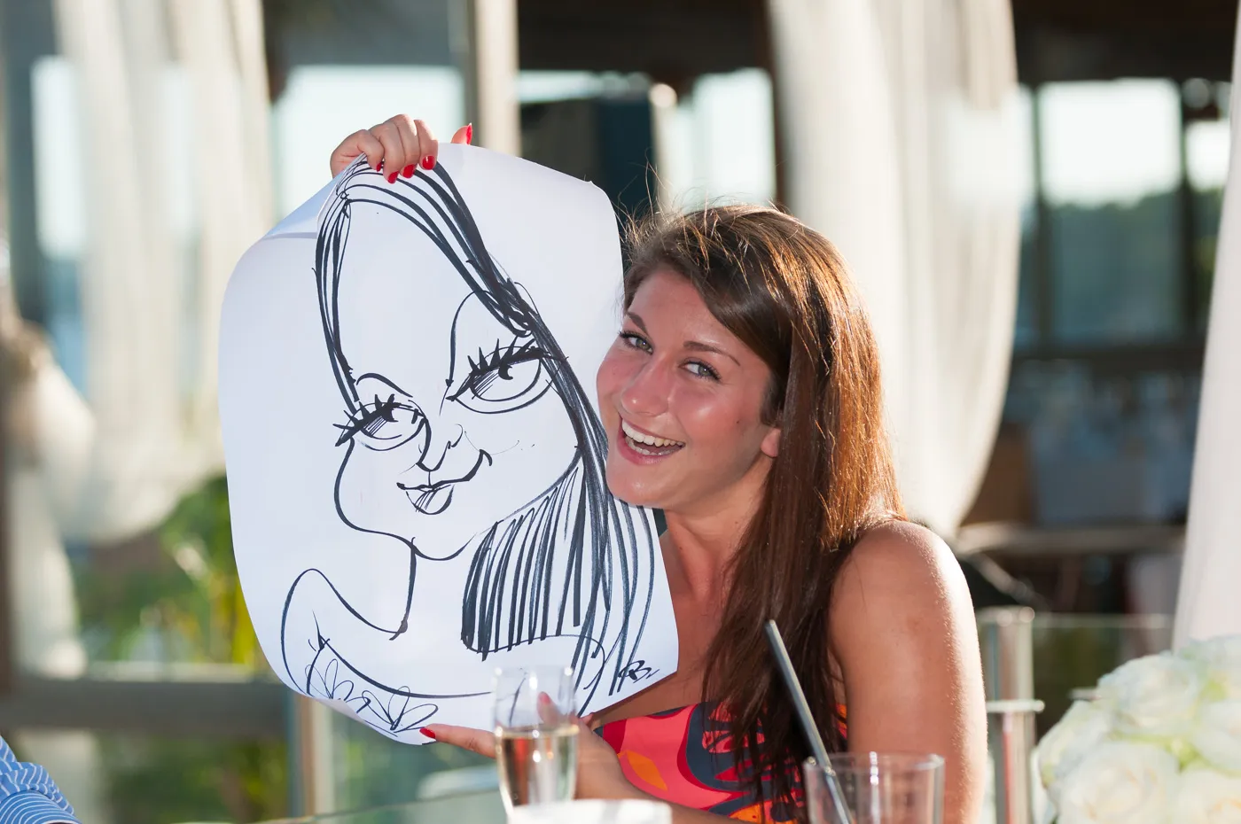 Smiling woman with long brown hair holding a caricature drawing of a woman with exaggerated facial features.