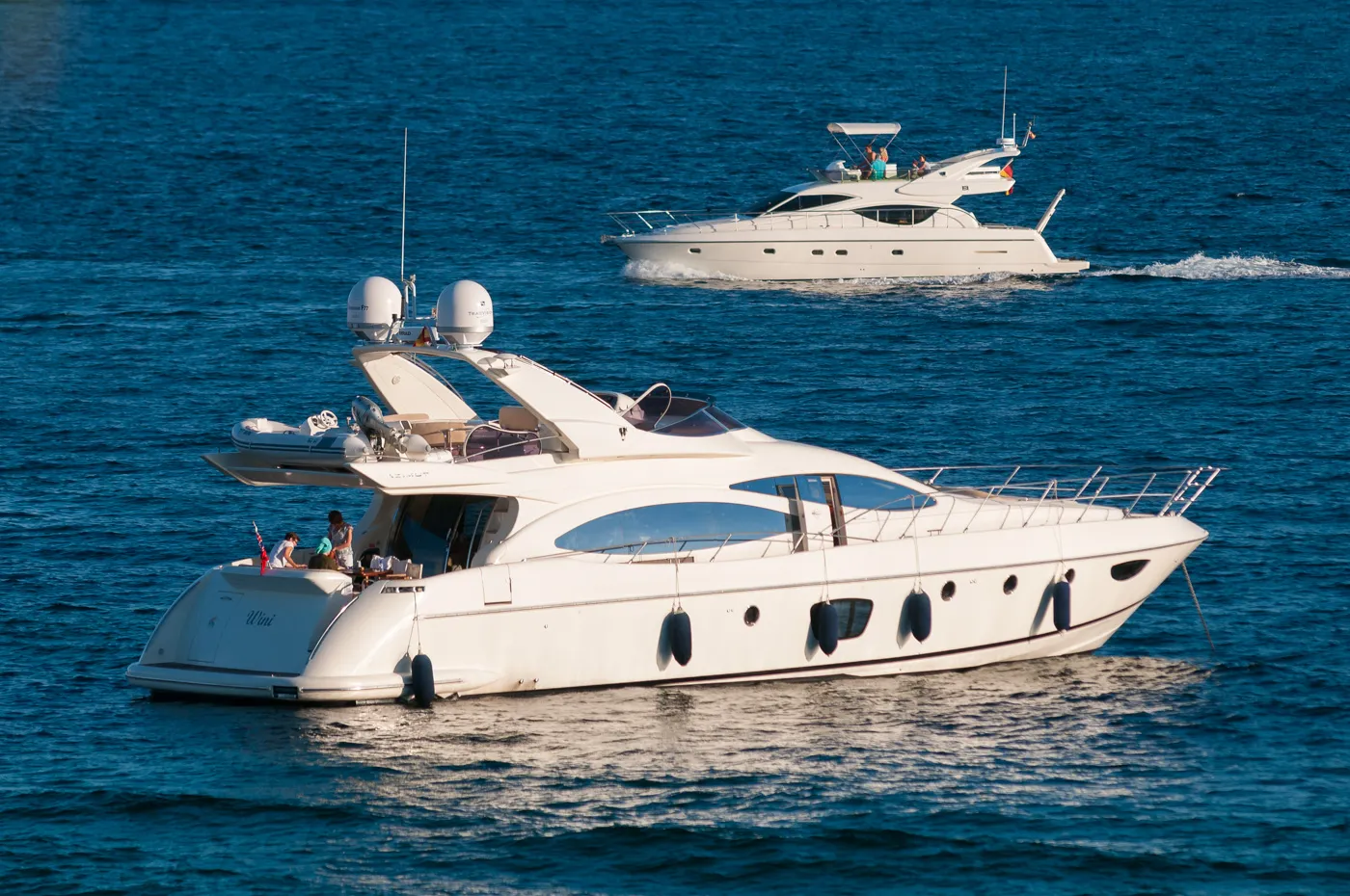 Two white luxury yachts on calm blue water, with people visible on each boat.