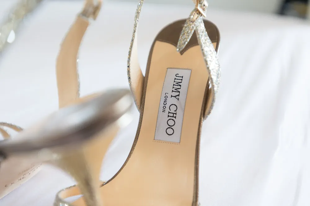 Close-up of inside sole of a glittery gold Jimmy Choo high-heeled sandal on a white surface.