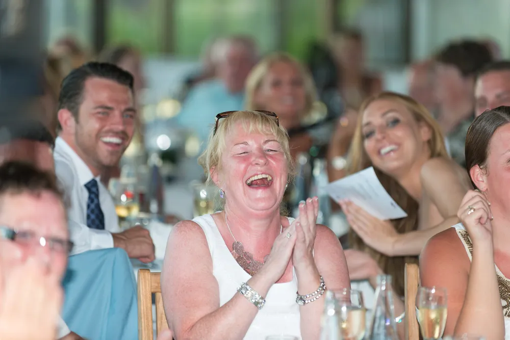 Group of people laughing and clapping while seated at a table during a social event.
