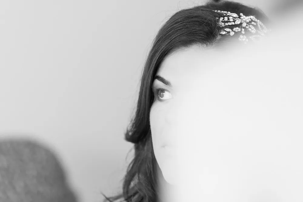 Black and white close-up of a woman with dark hair wearing a jeweled hair accessory, partially obscured by a blurred foreground.