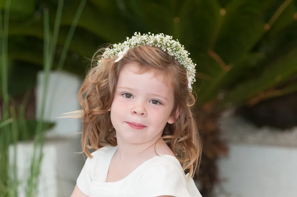Young girl with curly light brown hair wearing a white dress and a floral crown with white baby's breath flowers.