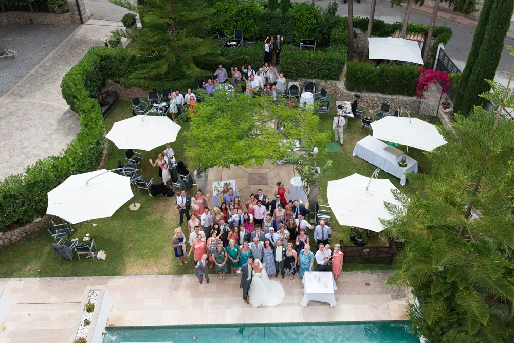 A large group of people posing for a photo in a garden area with white umbrellas and a swimming pool visible at the bottom.